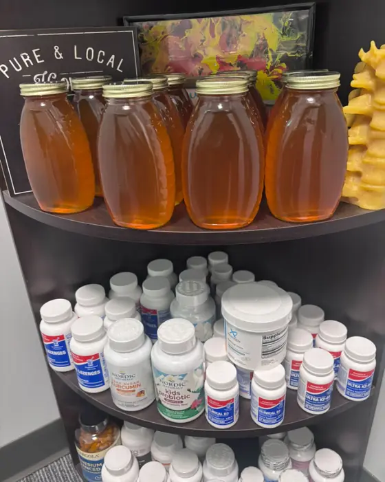 Jars of raw, local De Koyer Honey on the office shelf above a row of supplements