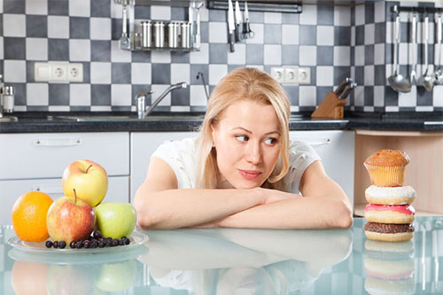 A woman choosing what to eat between fruits and sweets